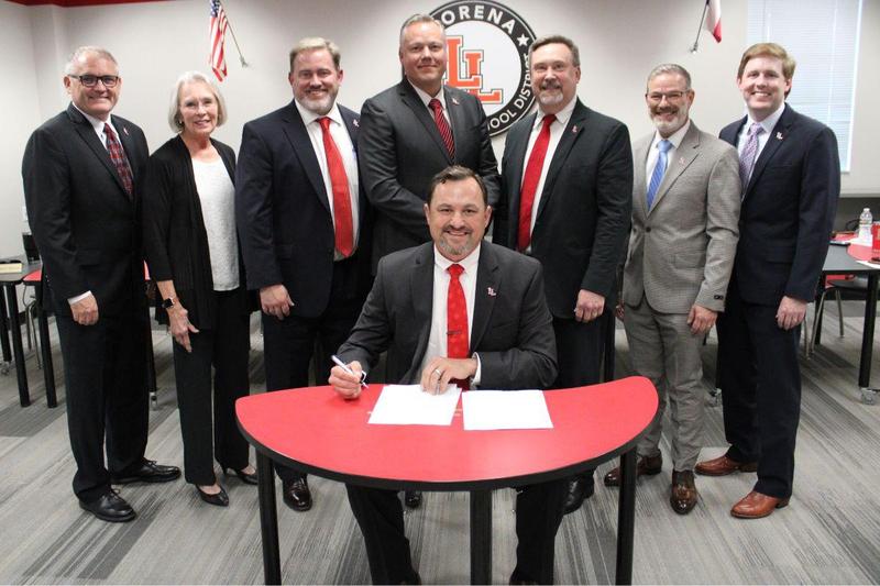Dr. Teddy Clevenger signing contract with school board members standing behind him