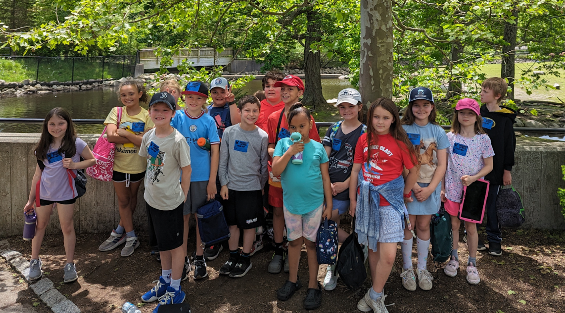 Group of children posing together outdoors near a pond.