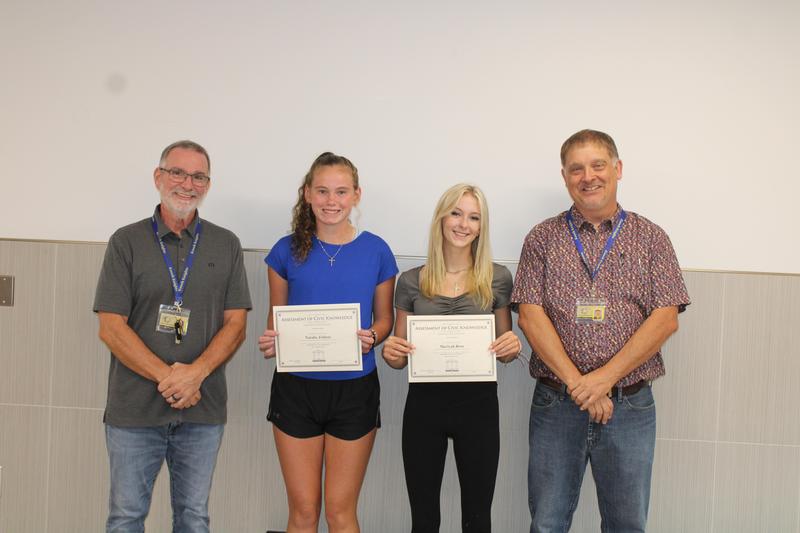 two girl students hold certificates while two male teachers stand beside them