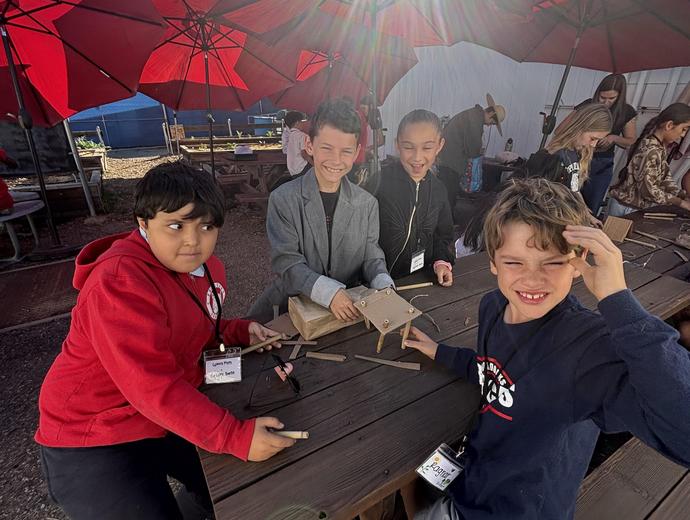 Four children smiling while working on a craft project under red umbrellas.