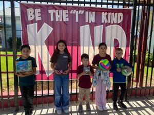 Students holding a toy, standing on the Be the "I in the kind background