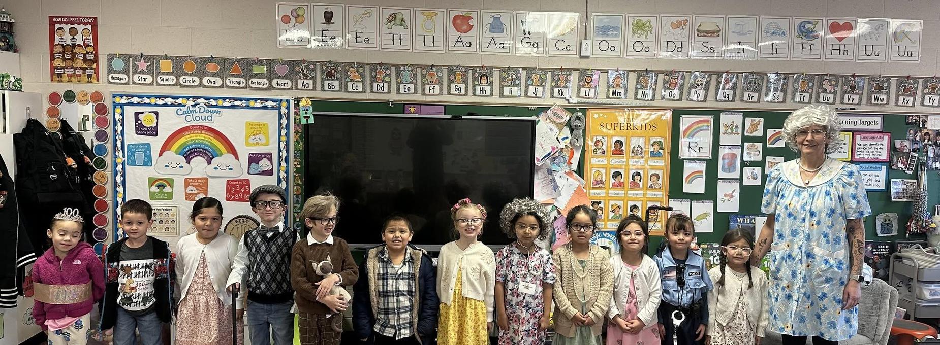 A classroom with students in costumes posing with a female teacher.