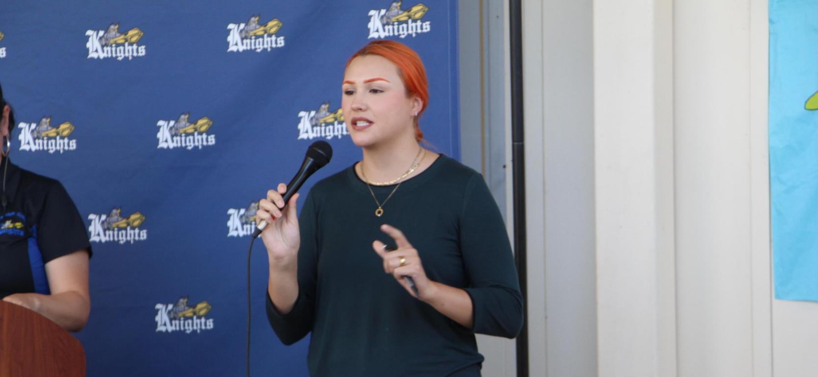 Person with orange hair speaking into a microphone at an event.