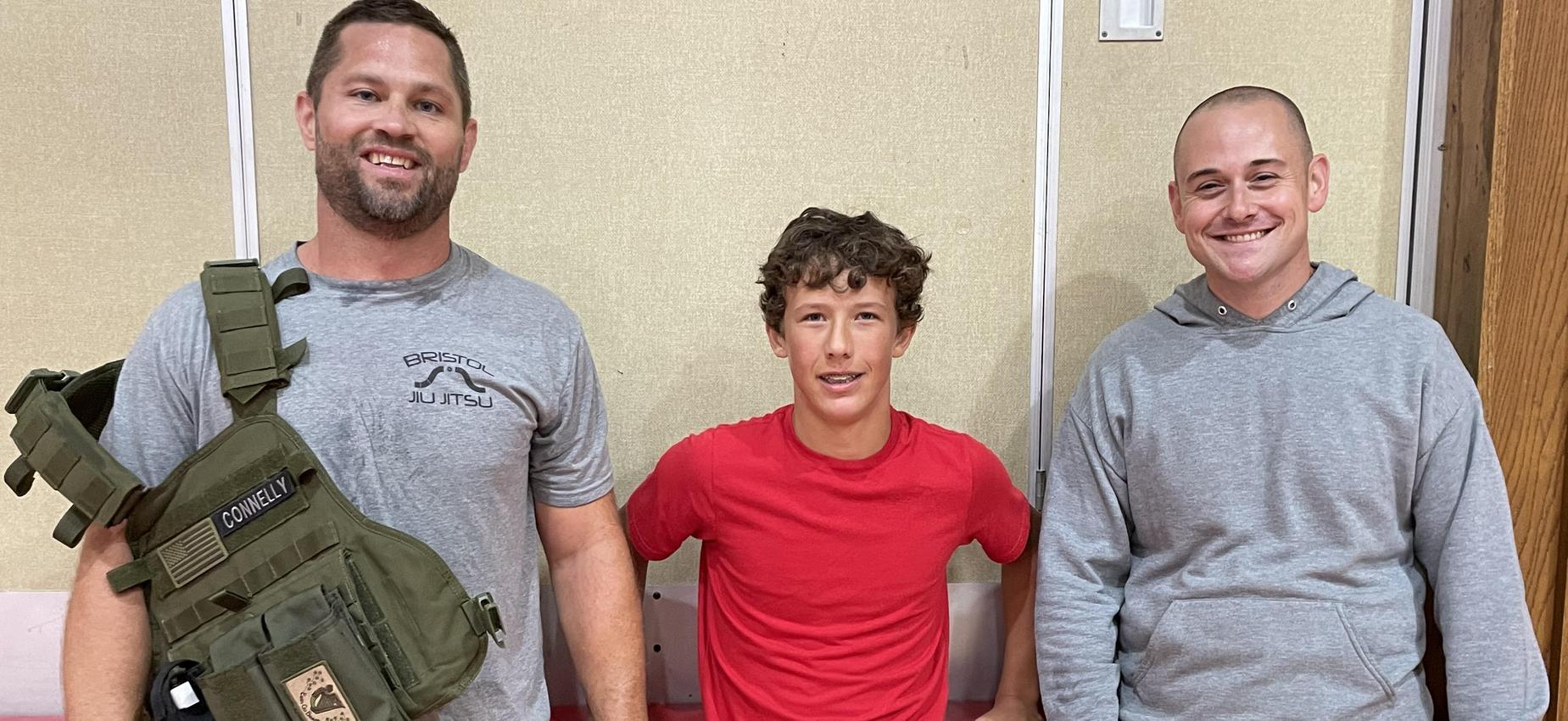 Two men stand with a student in a gym.