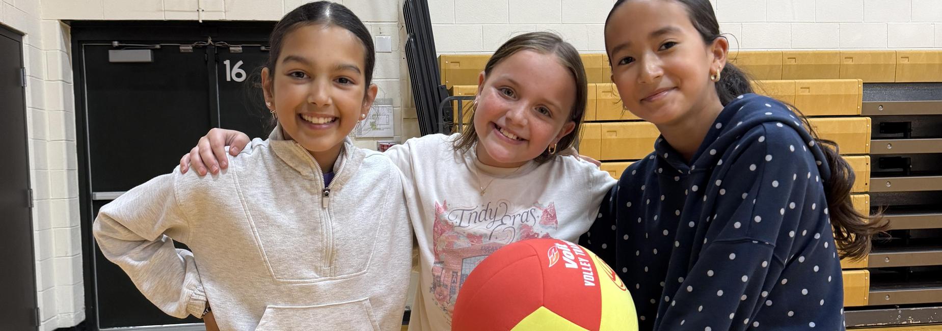 3 students smile with a volleyball