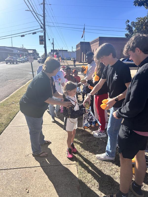 Elementary students on sidewalk, lining up to get candy or a football