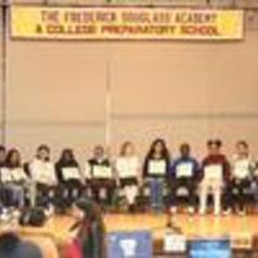 Students seated at a stage with signs, representing a school event.