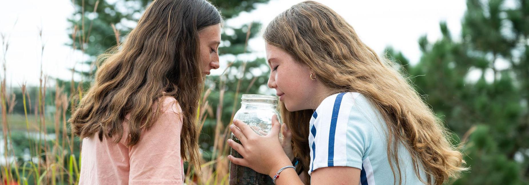 Two girls intently examining a jar together outdoors.