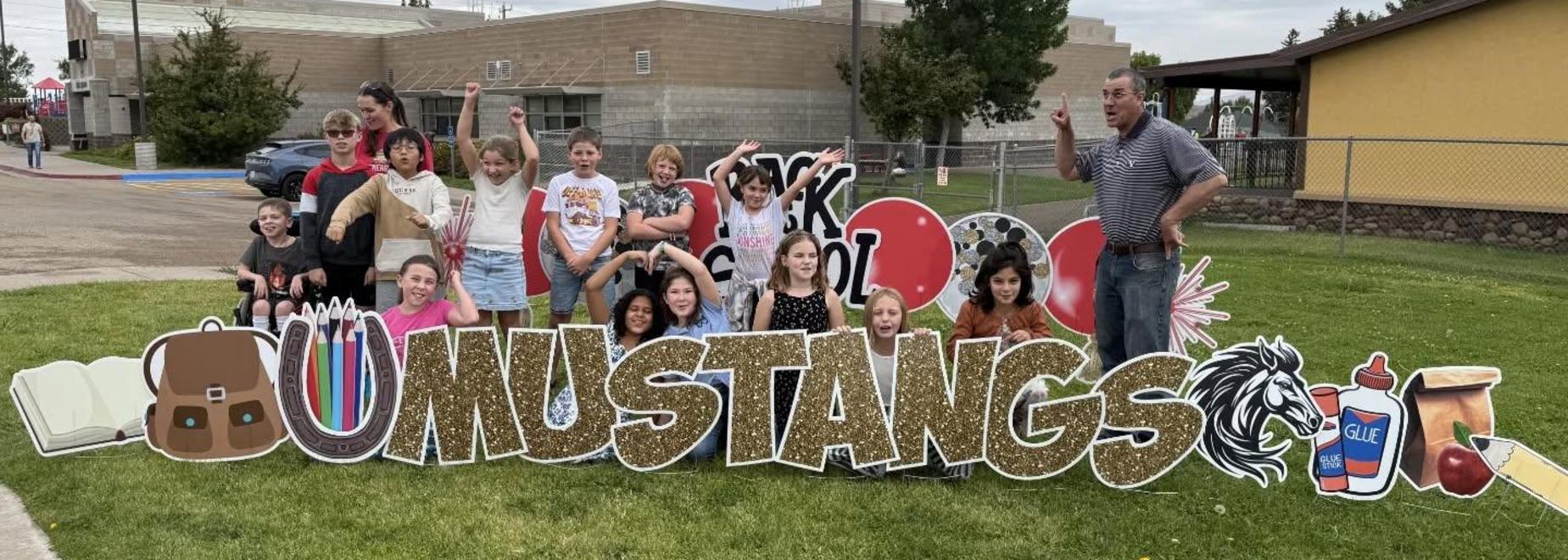 A diverse group of children posing playfully in front of a colorful school sign.