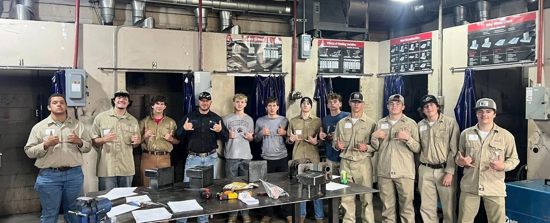 Group of welding students posing with their projects in a workshop setting.