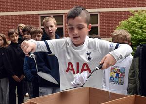 A boy using two utensils to pull shredded paper from a cardboard box surrounded by peers.
