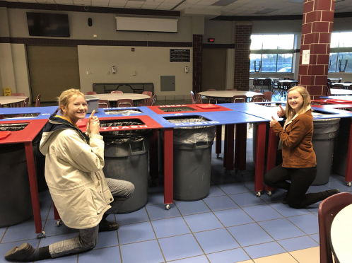 two girls bend down by recycling table in cafeteria
