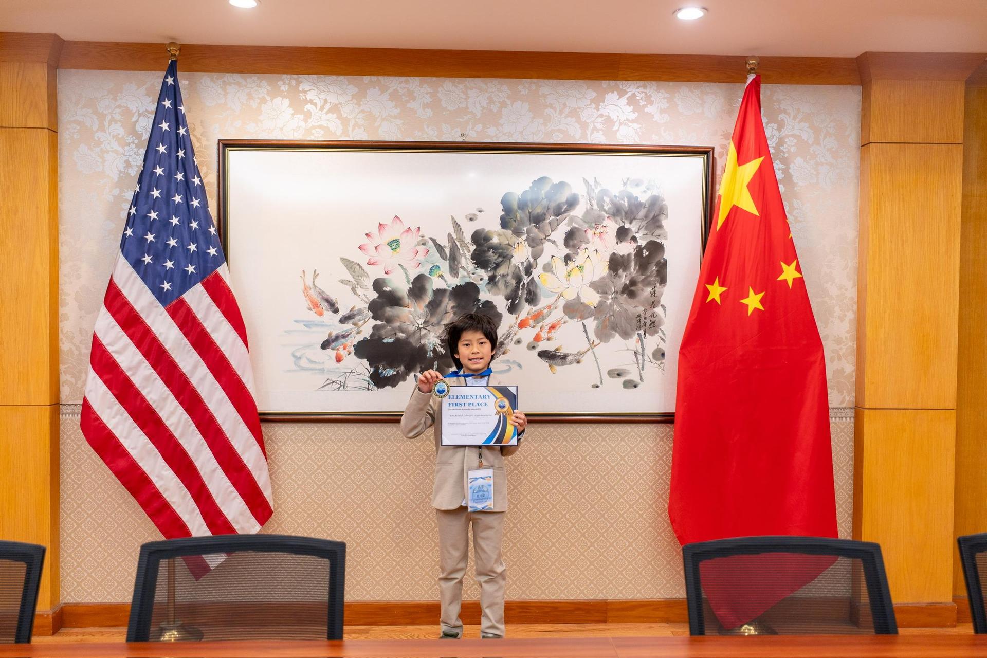 Thanachrid standing with a 1st place certificate in between the US flag and the Chinese flag