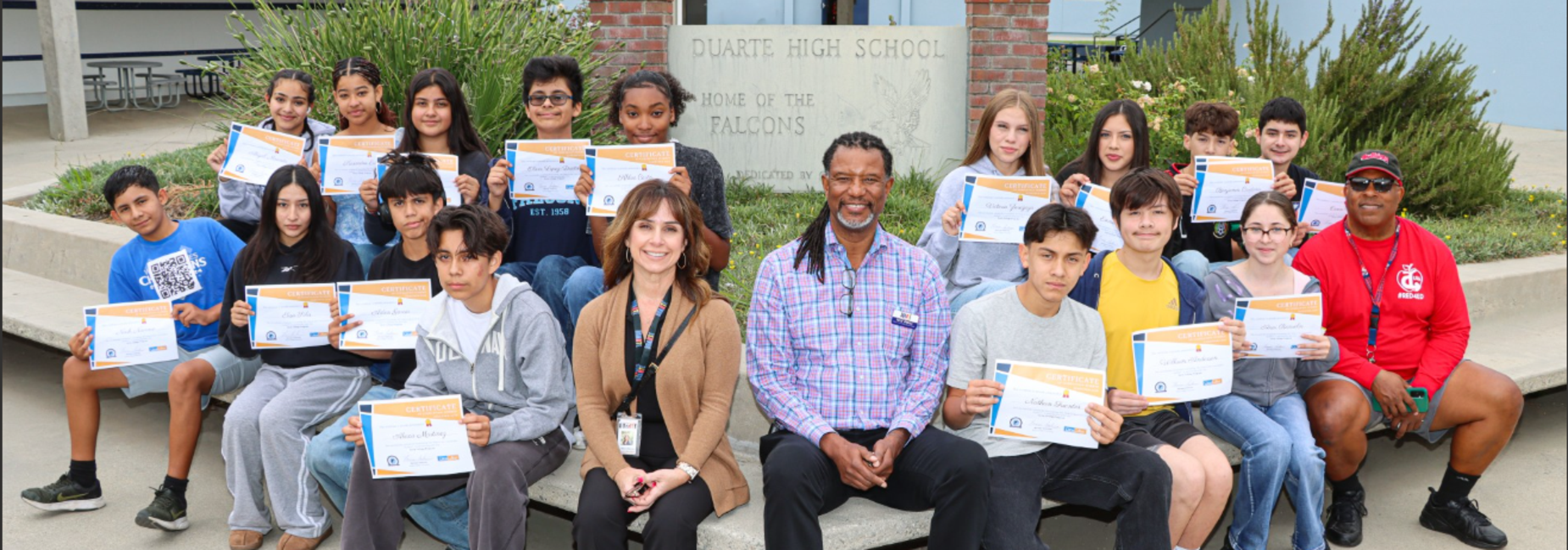 Group of students holding certificates with teachers outdoors.