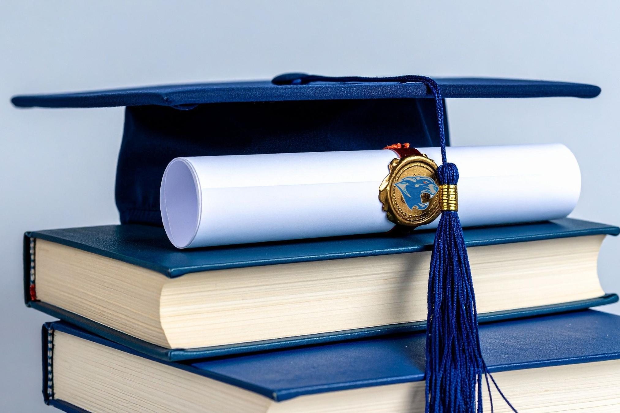 graduation cap and diploma sitting on stack of books