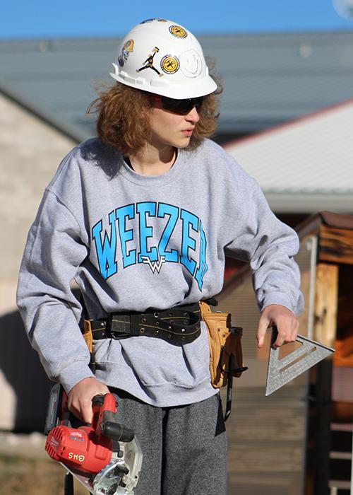 A student holds a saw and a triangle.