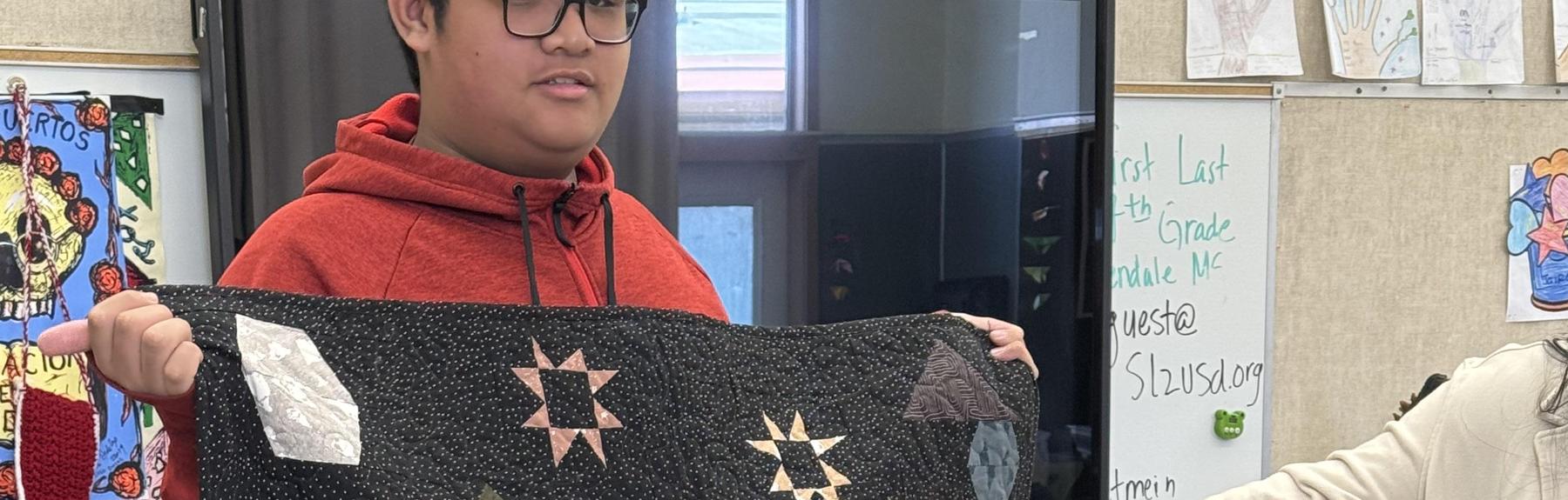 Student holding up a quilt.