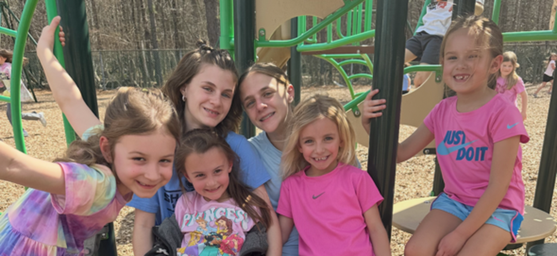 Group of girls smiling while sitting on playground equipment.