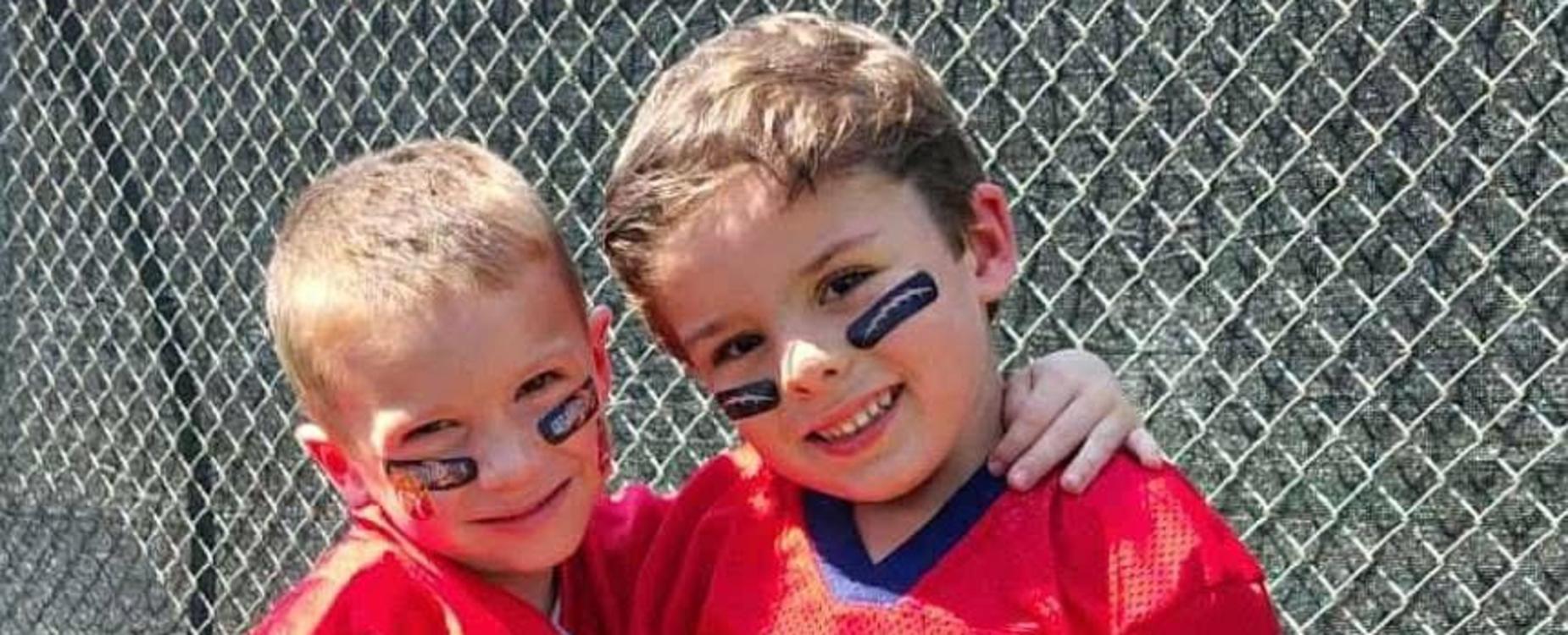 Two children in red t-shirts posing together with a grassy background.