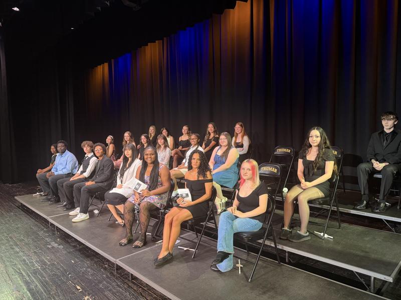 Juniors and seniors sit on the auditorium stage.