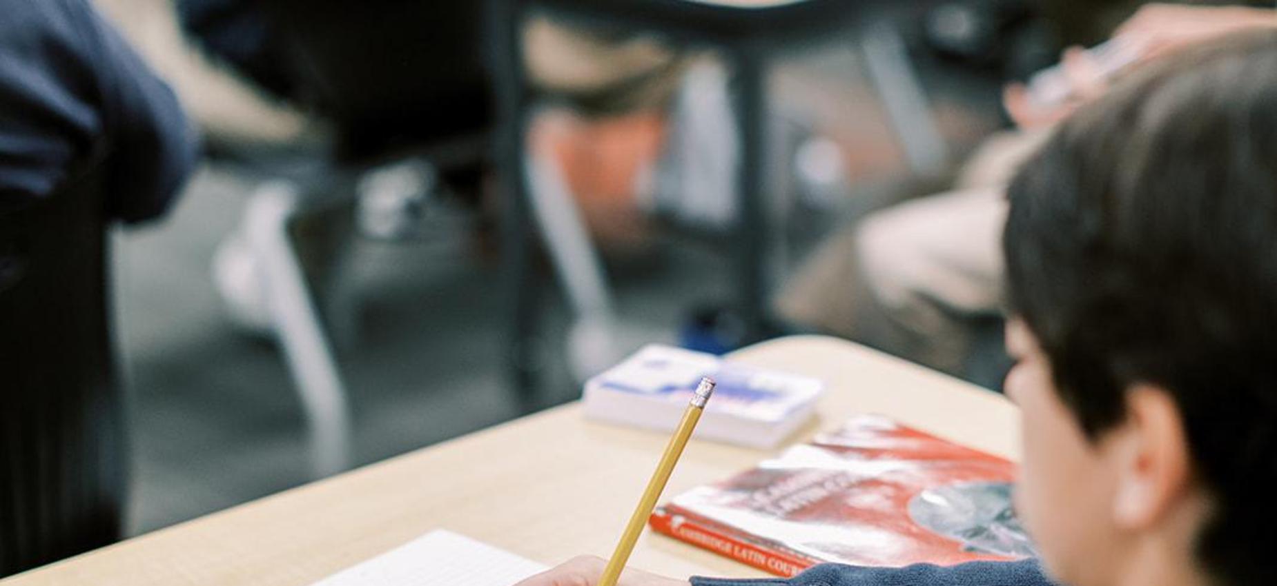 Student writes in a notebook at his desk