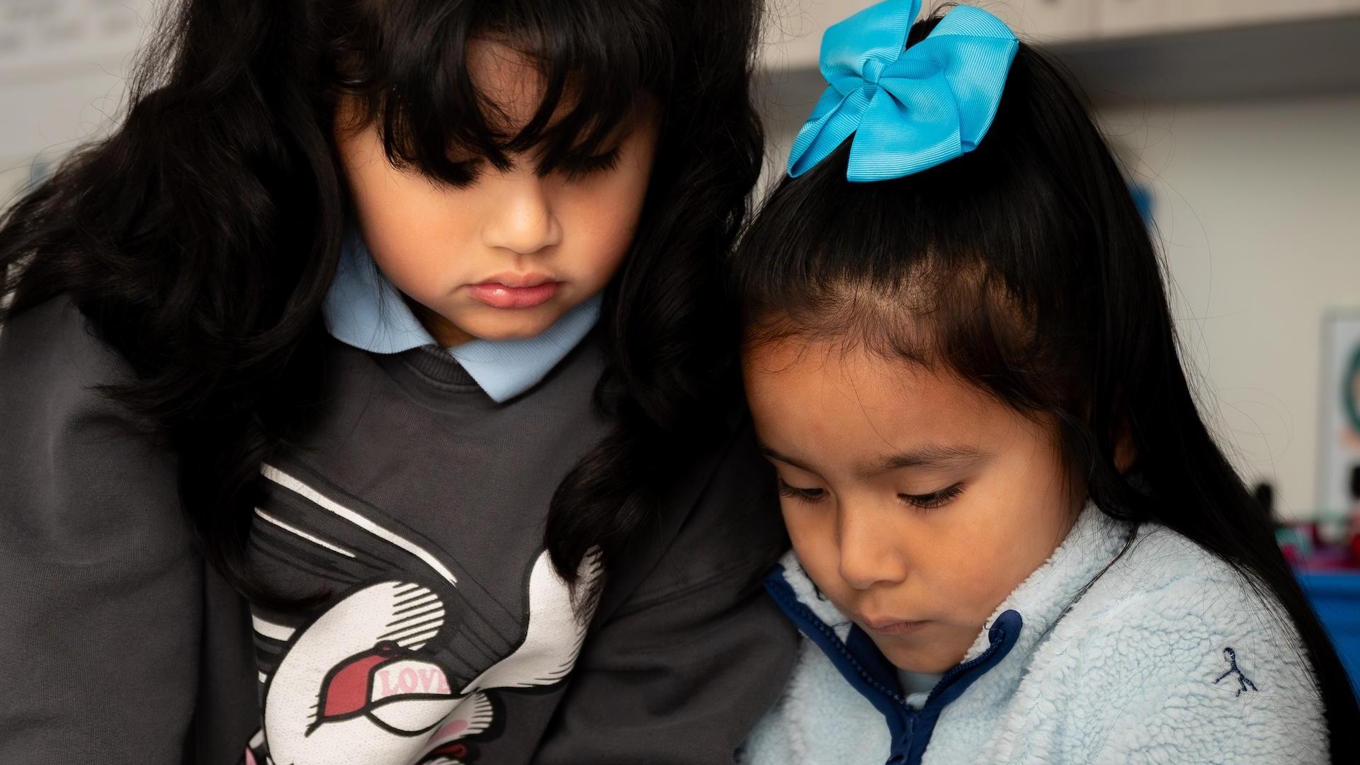 Two children focused on an activity, one wearing a gray sweatshirt and the other a blue fleece.