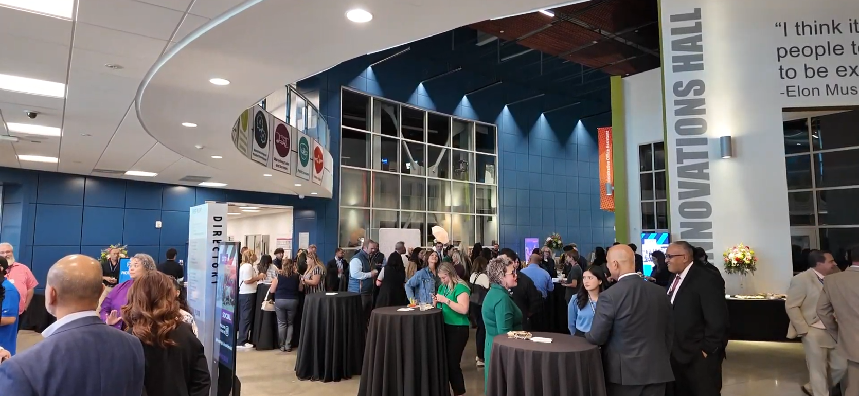 Crowd gathered at an event in a modern venue with cocktail tables.