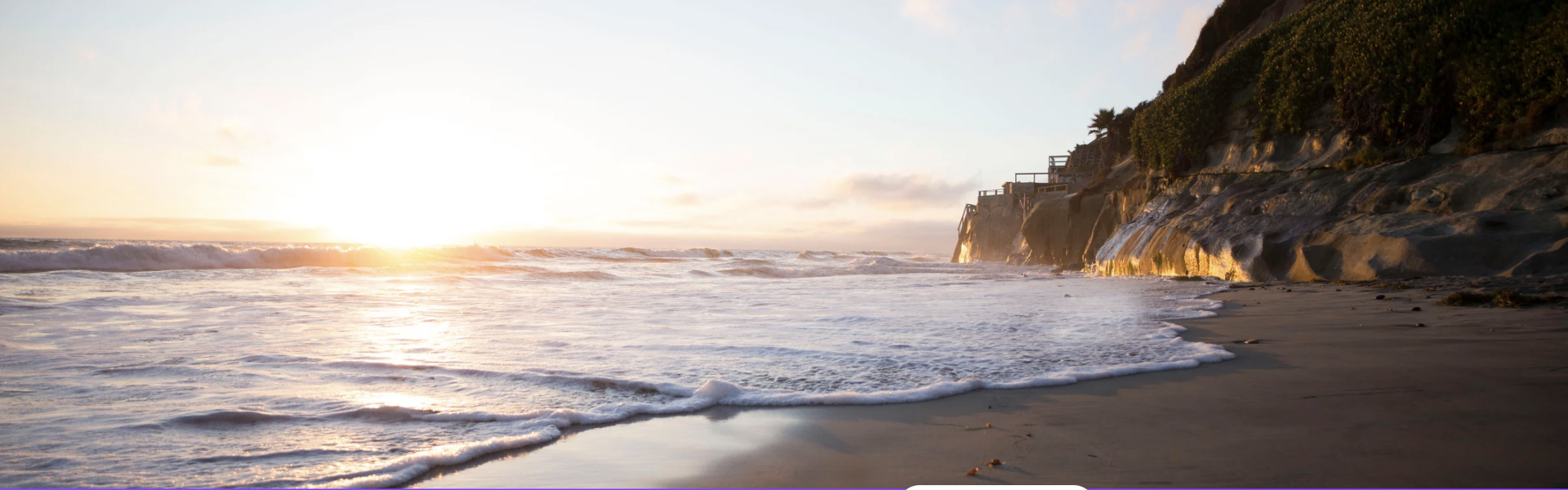 A California beach at sunset with foamy ocean water gliding over the sand