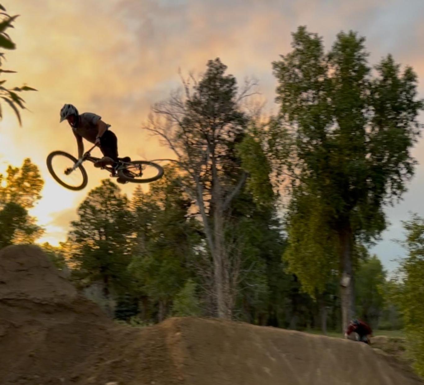 A cyclist performing a jump off a dirt ramp at sunset.