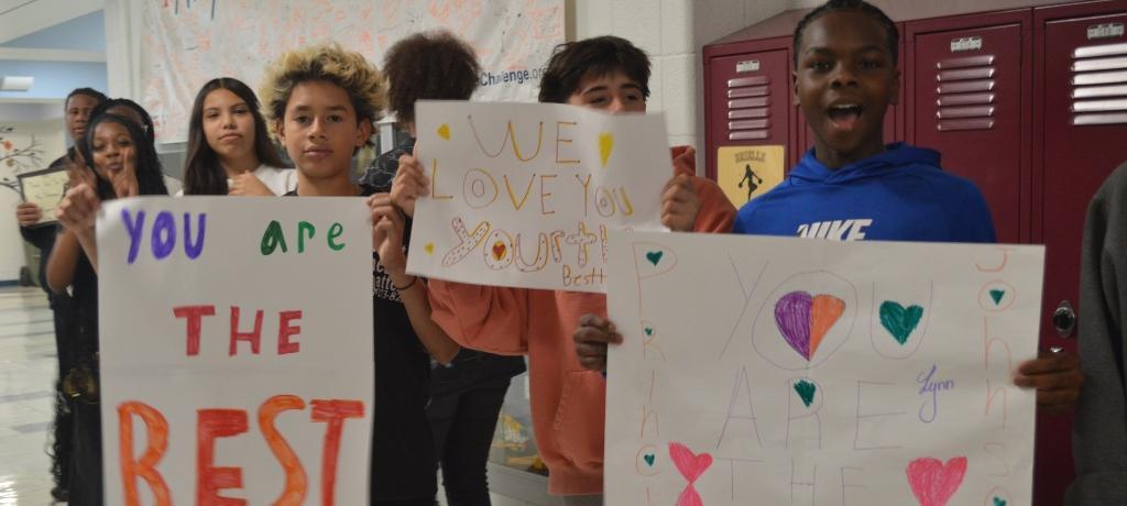 students with "you are the best" signs line a hallway