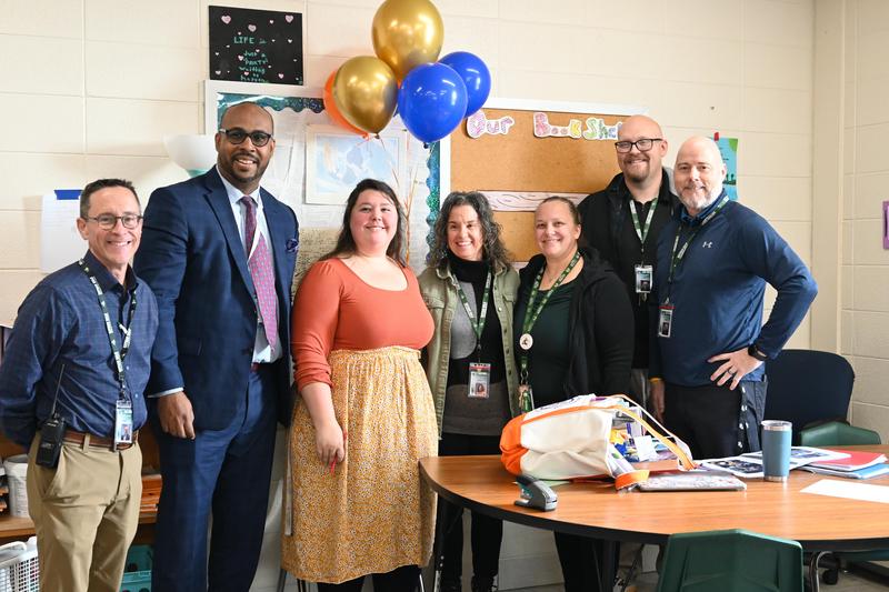 A group of six people celebrating with balloons in a classroom setting.
