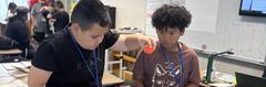 Two boys engaging with a project, one holding an object while the other observes.