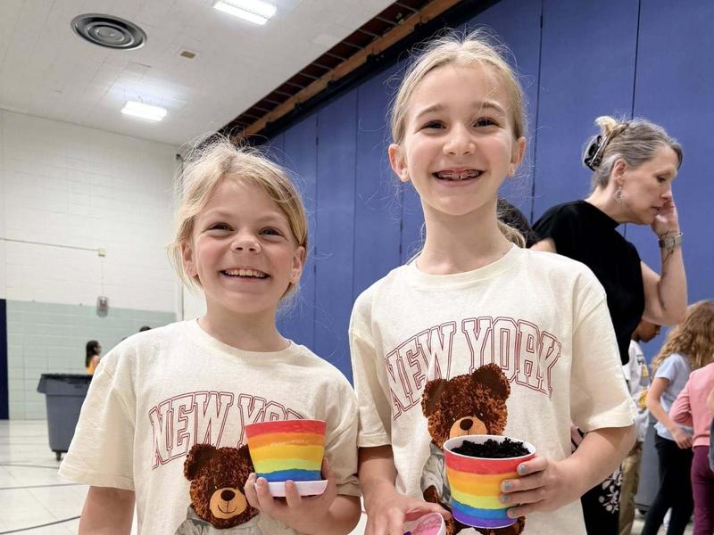 Two girls in matching bear-themed shirts holding colorful pots.