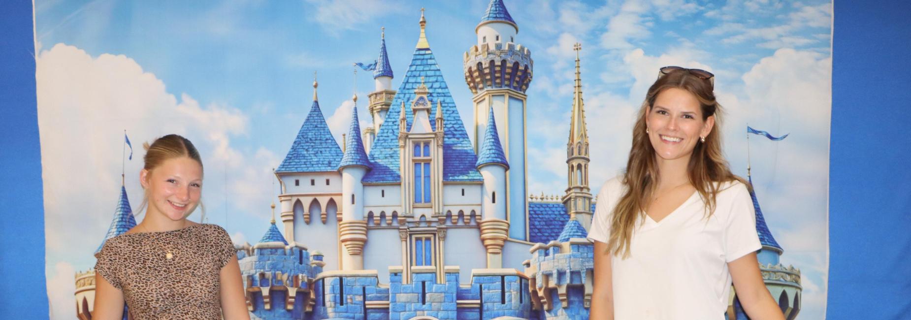 Two women posing with castle towers in front of a blue castle backdrop.
