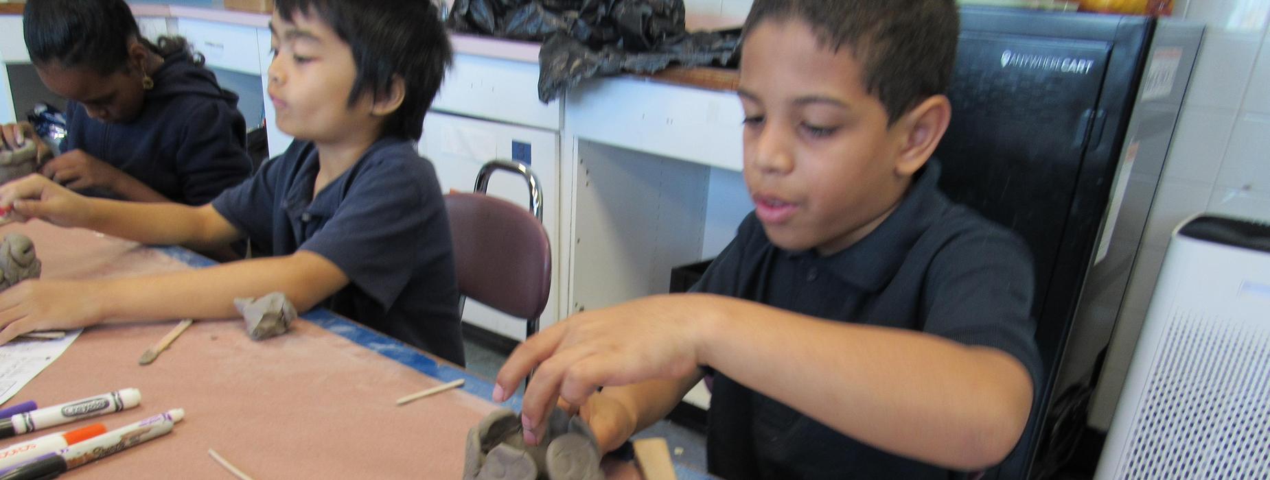 A child shaping clay with hands on a workbench covered in art supplies.