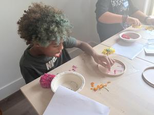 a student picking pink petal out of a dish with a pink flower resting on the table.