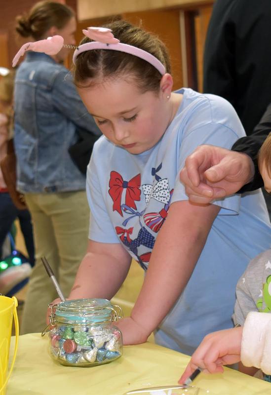 Young girl with bunny ears examines a jar of colorful treats at a festive event.