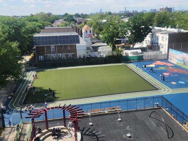 Aerial view of a sports field with synthetic grass, surrounded by buildings and trees.