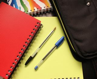 Two pens on a bright yellow sheet near various notebooks.