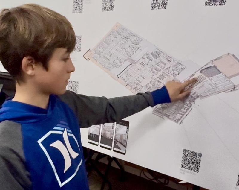 A youth examines a poster containing an architectural drawing of a proposed school building.