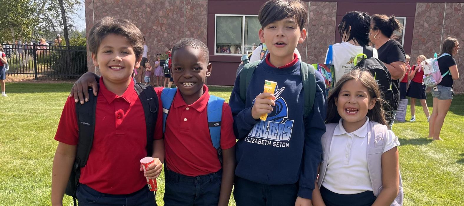 Four children smiling outdoors, holding treats after an event.