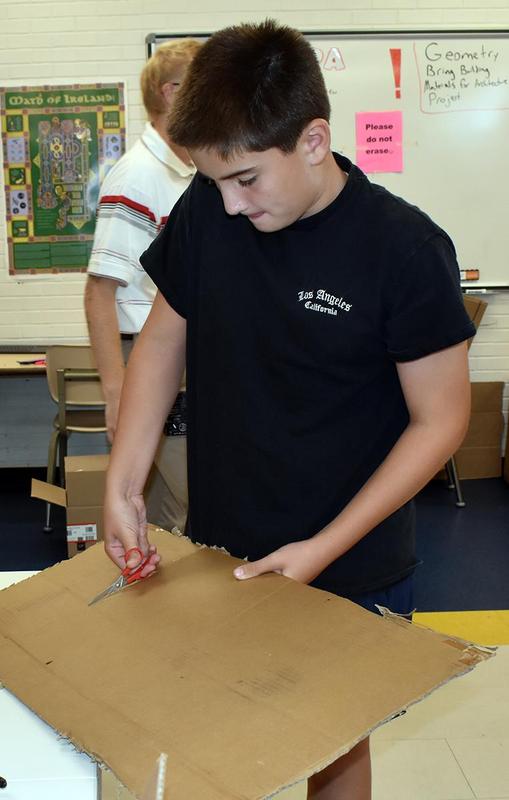 A boy cutting cardboard with scissors at a table.