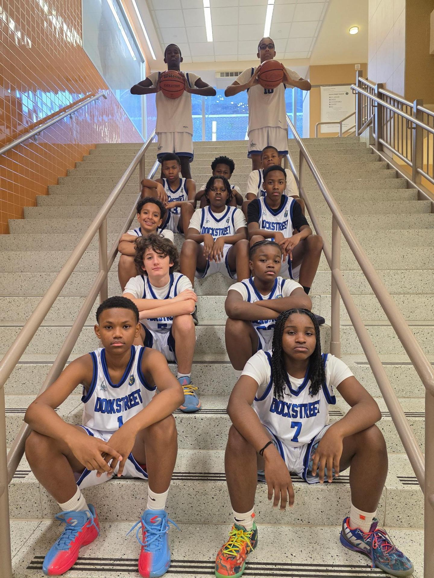 Basketball team in jerseys posing with a basketball indoors.