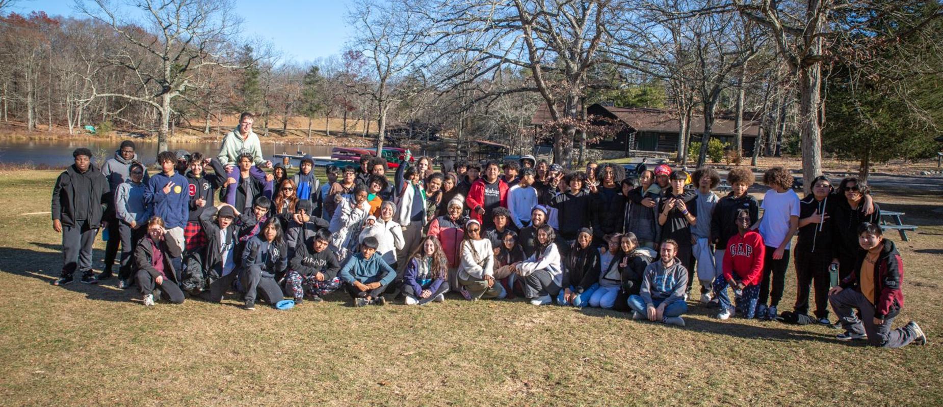 Group of diverse people gathered outdoors near a lake on a sunny day.