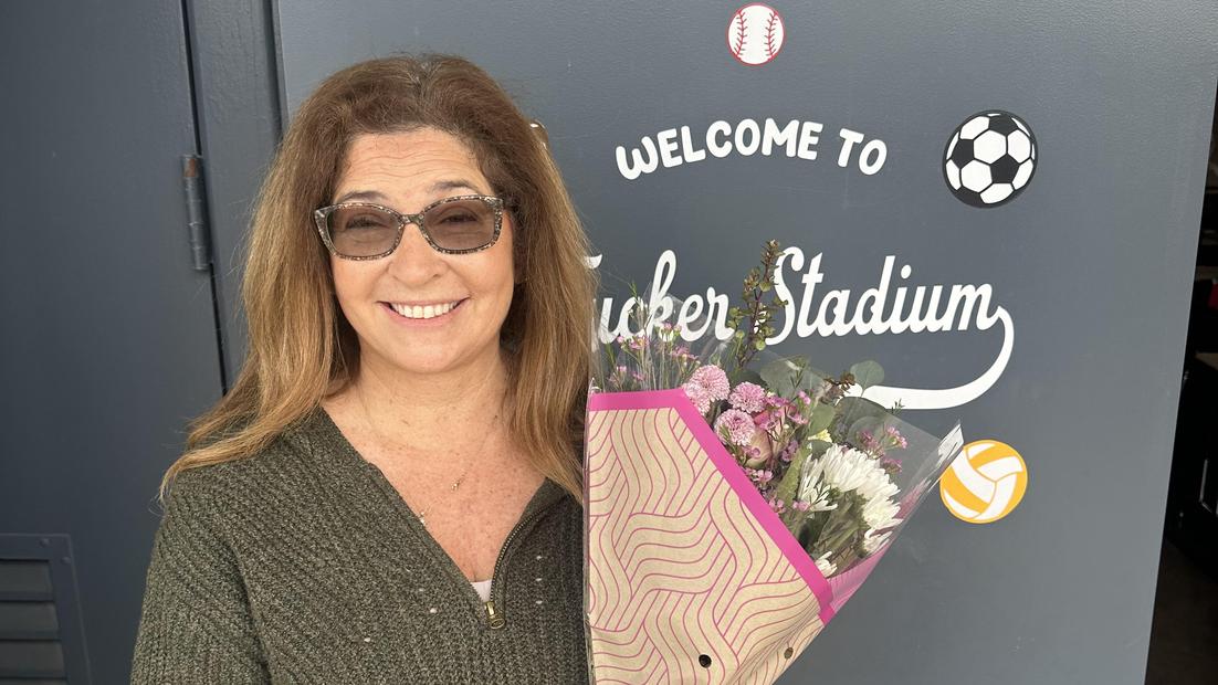 Woman smiling and holding a bouquet of flowers at Tucker Stadium entrance.