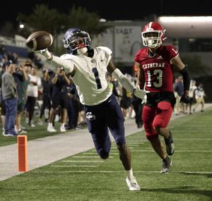 A football player stretches to catch a pass while another player defends.