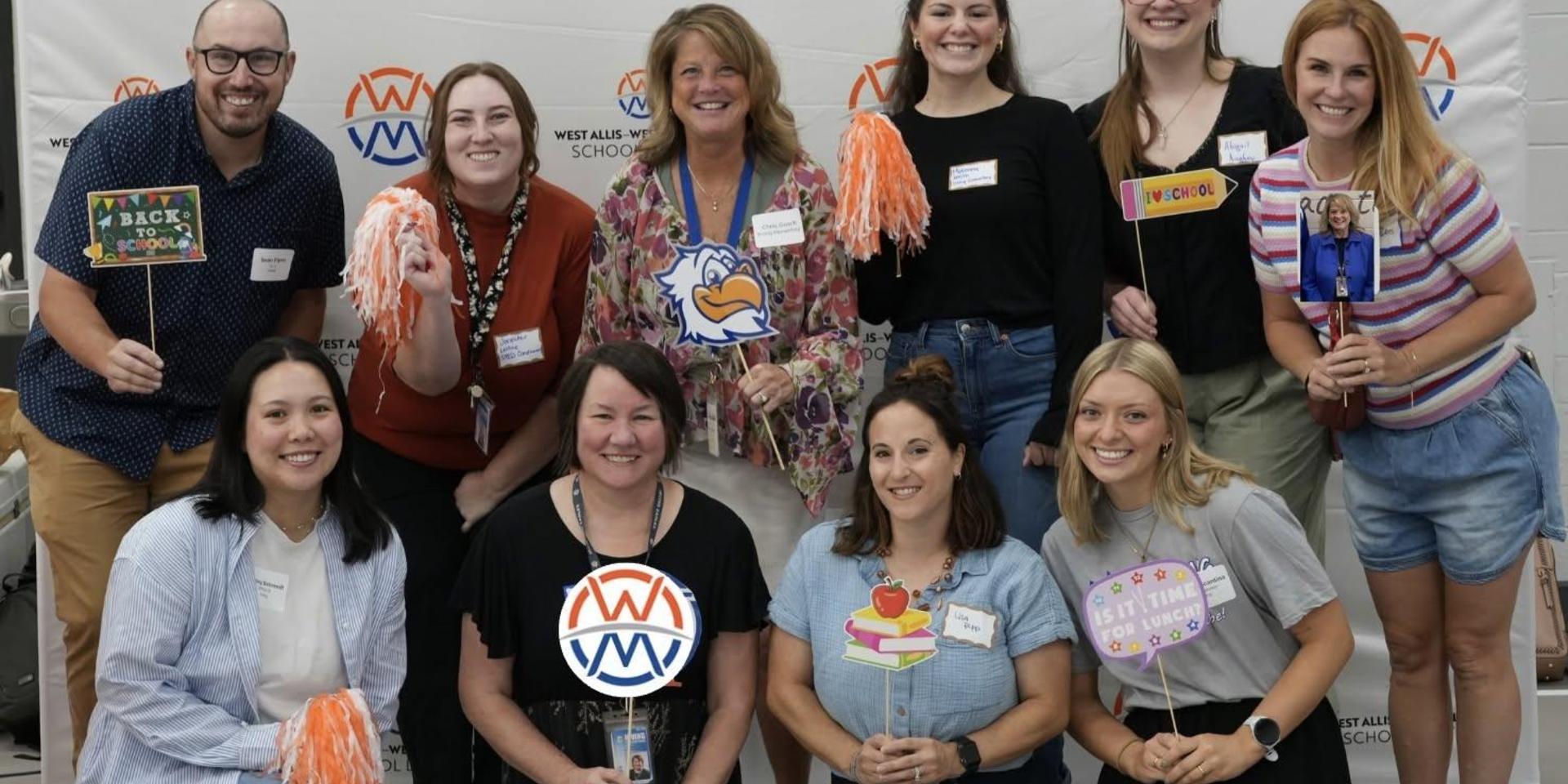 Group of smiling adults holding fun props at a school event.