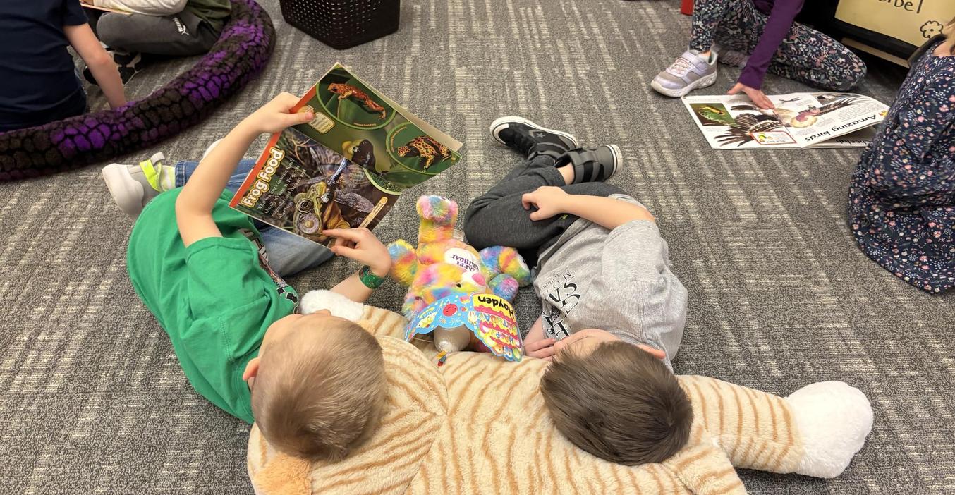 Two students lay on a stuffed animal as they read together.