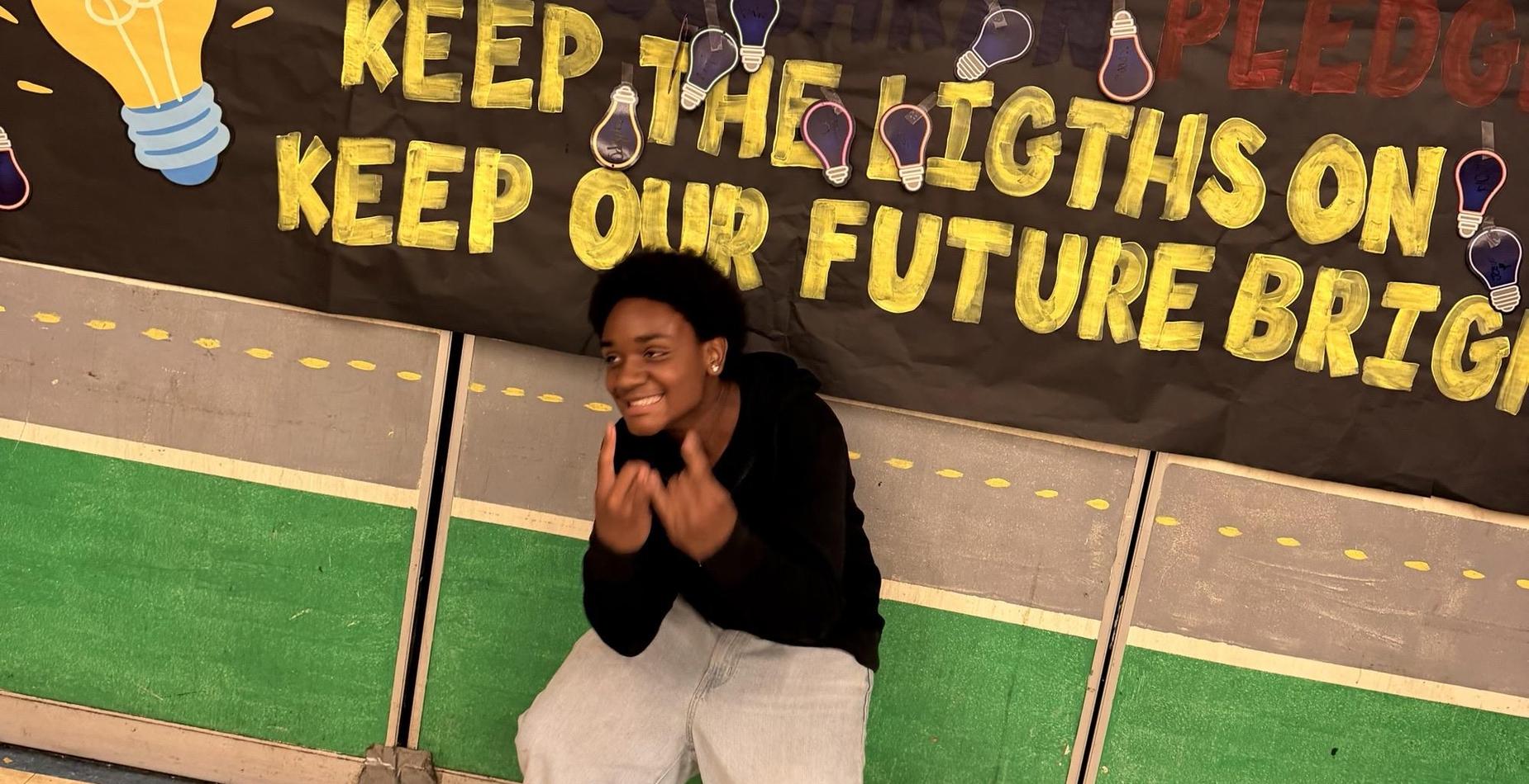 Student smiling in front of the Cochran Pledge banner: Keep the lights on, keep our future bright.