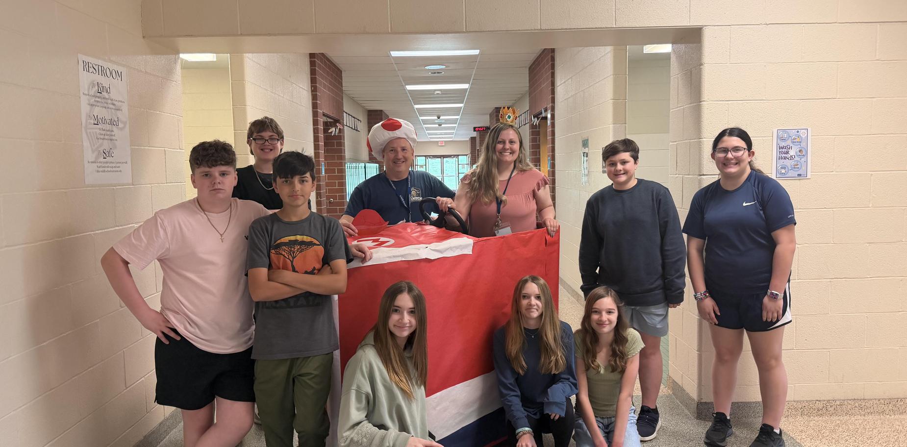 A group of students and adults, including a man in a Santa hat, in a hallway.
